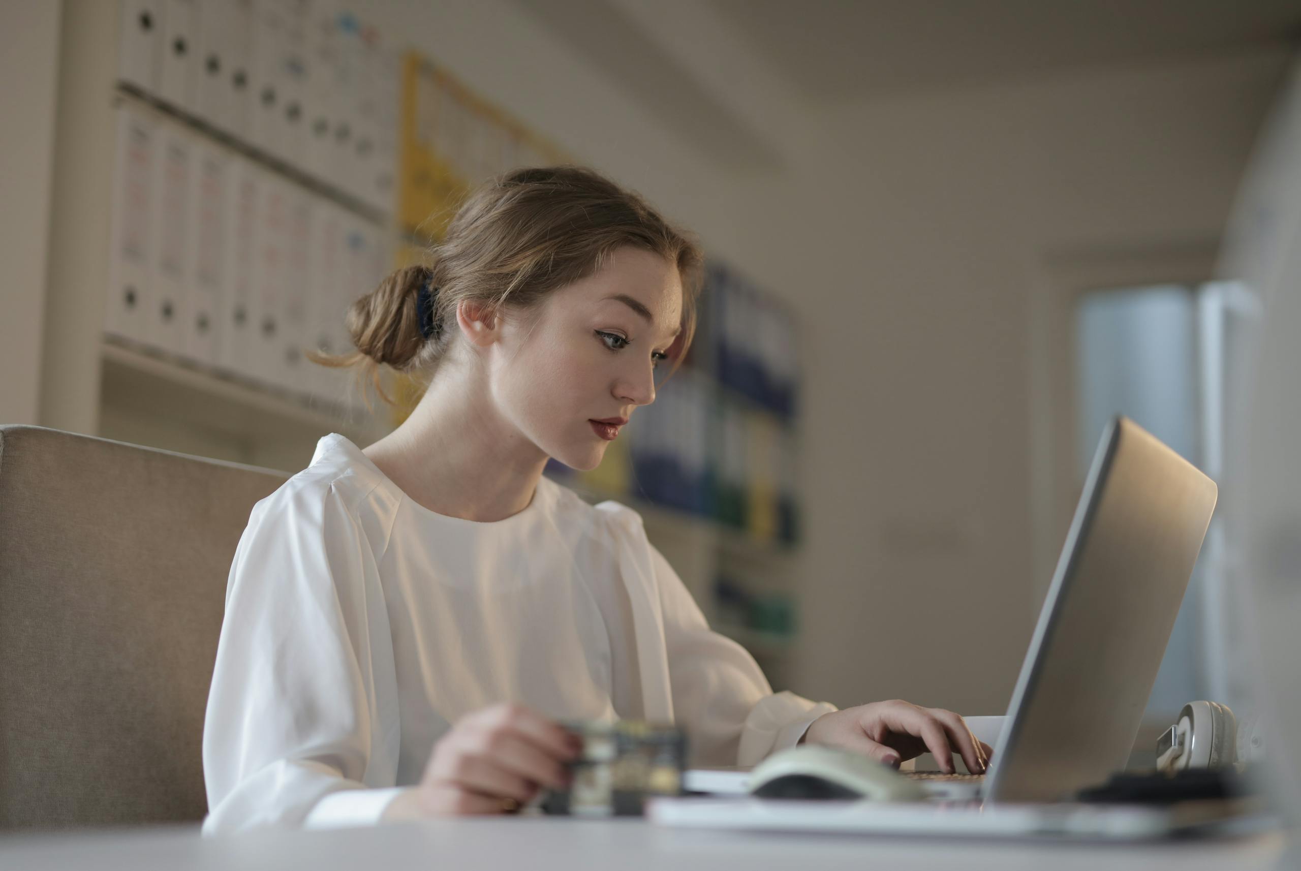 Focused young woman working remotely on a laptop in a modern office.